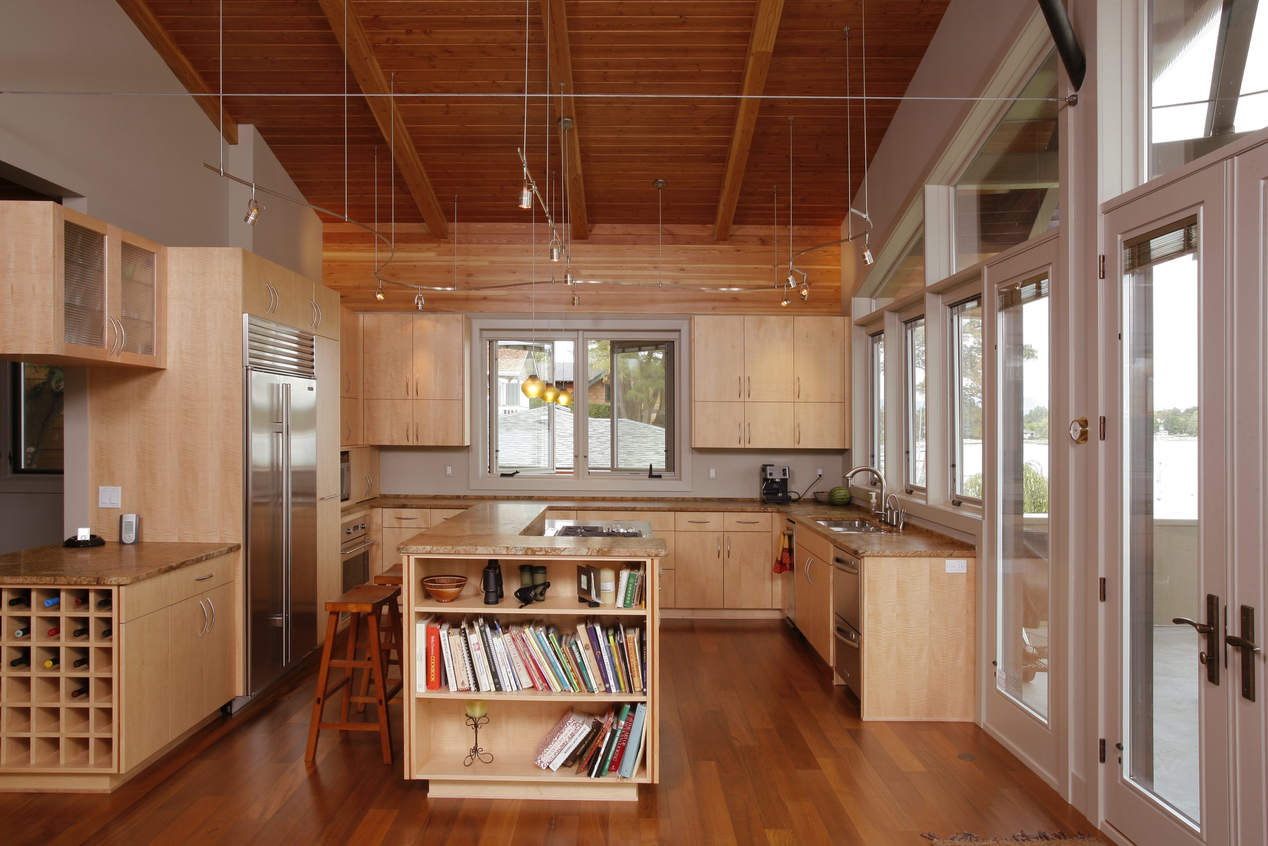 Photo of natural wood kitchen including countertops, island with built-in shelves and wine rack. Windows pictured and left side of back door.